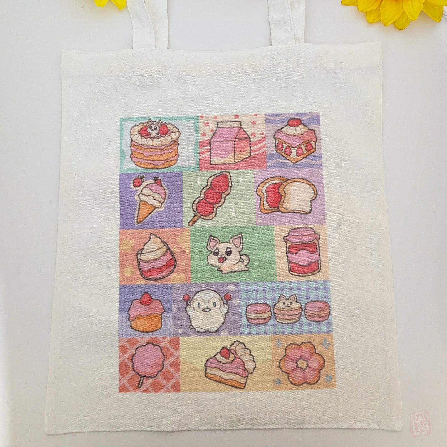 Cute pastel dessert-themed tote bag featuring original Radlab characters  surrounded by cakes, macarons, ice cream, pastries, and café-inspired artwork. Reusable 14 x 16 inch canvas polyester tote bag for shopping, school, conventions, and everyday use.
