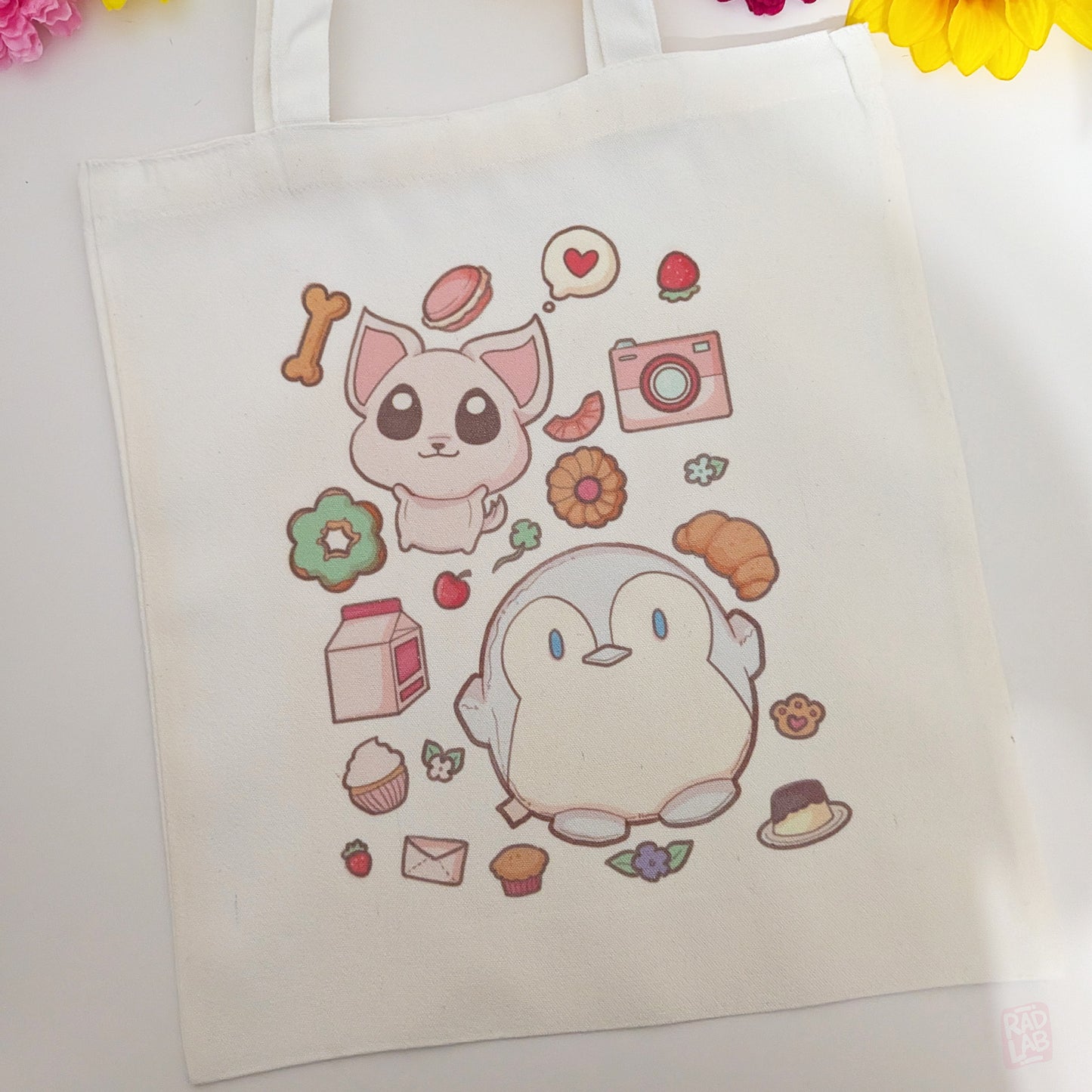Cute pastel tote bag featuring original Radlab characters surrounded by sweets, flowers, snacks, and kawaii café-themed artwork. Reusable 14 x 16 inch canvas polyester tote bag for everyday use.