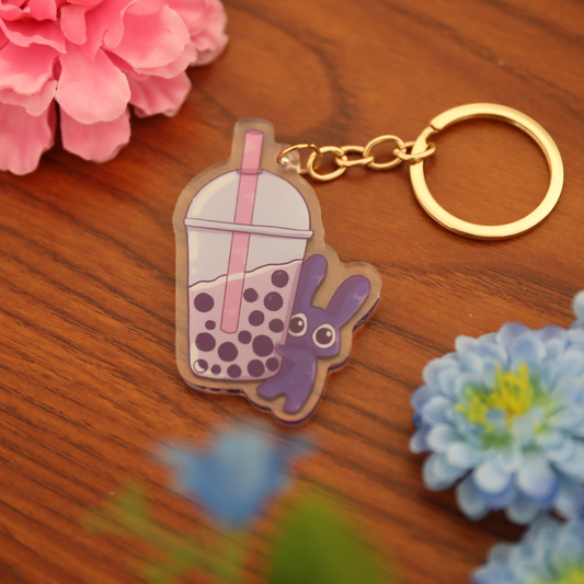 Keychain with a cartoon character inside a bubble tea cup on a wooden surface with flowers.